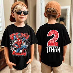 May include: Black t-shirt featuring a Spider-Man graphic with the text "It's My Birthday" and a checkered background. The back of the shirt displays a red number 2 with a spiderweb design and the name "Ethan".