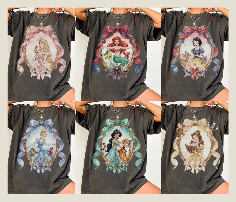 May include: Dark gray t-shirts featuring various Disney princess portraits within ornate frames. Each shirt showcases a different princess, including Aurora, Ariel, Snow White, Cinderella, Jasmine, and Belle, with detailed illustrations and colorful accents.