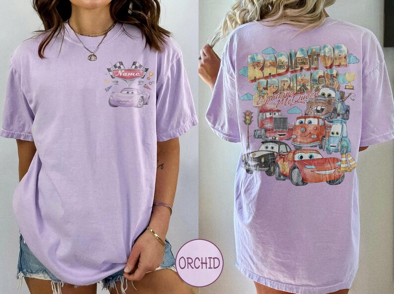 May include: A light purple t-shirt featuring a small graphic on the front chest with a race car and the text Name. The back displays a large, colorful illustration of various characters from the movie Cars with the text Radiator Springs Lightning McQueen.