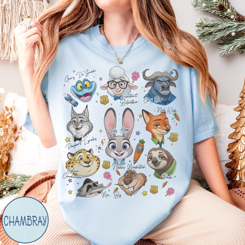 May include: Light blue t-shirt featuring cartoon illustrations of characters from a movie. The shirt includes images of a frog, sheep, buffalo, fox, rabbit, and sloth, with character names. The word "CHAMBRAY" is printed on the bottom left.