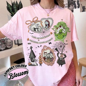 May include: Pink Comfort Colors t-shirt featuring illustrations from "The Nightmare Before Christmas." The design includes Jack Skellington, Sally, Oogie Boogie, and other characters in ornate frames. The text "The Nightmare Before Christmas" is also present.