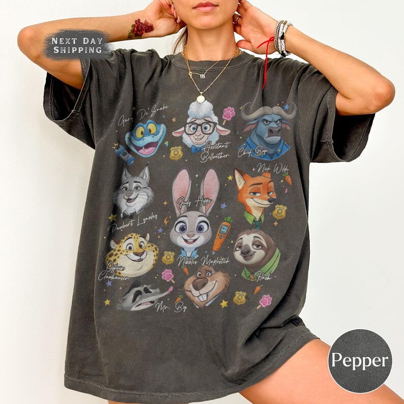 May include: Dark gray t-shirt featuring colorful cartoon character portraits with names. The shirt has a crew neck and short sleeves. The text "NEXT DAY SHIPPING" is at the top left. The shirt is labeled "Pepper" at the bottom right.