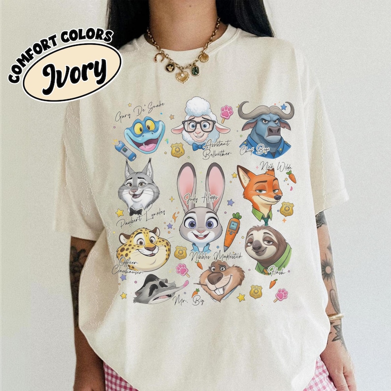May include: Ivory-colored t-shirt featuring cartoon characters from a movie. The design includes a frog, sheep, buffalo, wolf, rabbit, fox, cheetah, sloth, and other characters. The shirt has the words "COMFORT COLORS" and "Ivory" printed on it.