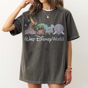 May include: Dark grey t-shirt with a Walt Disney World graphic. The design features a castle, tree, and Spaceship Earth, with the words "Walt Disney World". The shirt has a vintage, worn appearance.