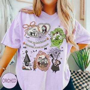May include: A light purple t-shirt featuring a graphic design from "The Nightmare Before Christmas." The design includes characters like Jack Skellington, Sally, and Oogie Boogie in ornate frames, with the text "The Nightmare Before Christmas."