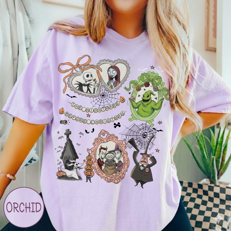 May include: A light purple t-shirt featuring a graphic design from "The Nightmare Before Christmas." The design includes characters like Jack Skellington, Sally, and Oogie Boogie in ornate frames, with the text "The Nightmare Before Christmas."