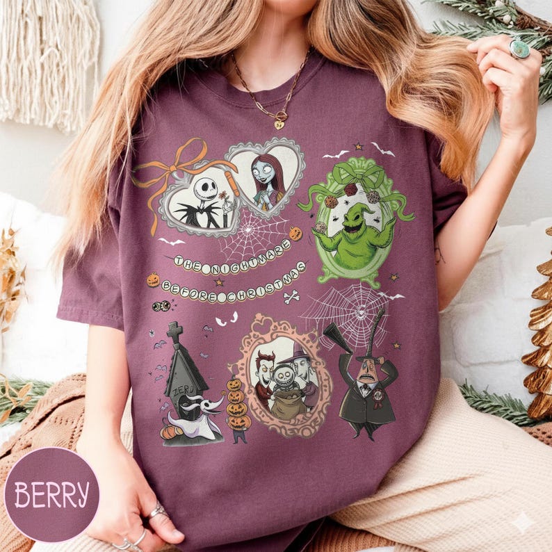 May include: Berry-colored t-shirt featuring multiple framed illustrations of characters from "The Nightmare Before Christmas." The illustrations include Jack Skellington, Sally, Oogie Boogie, and Zero. The text "The Nightmare Before Christmas" is also present.