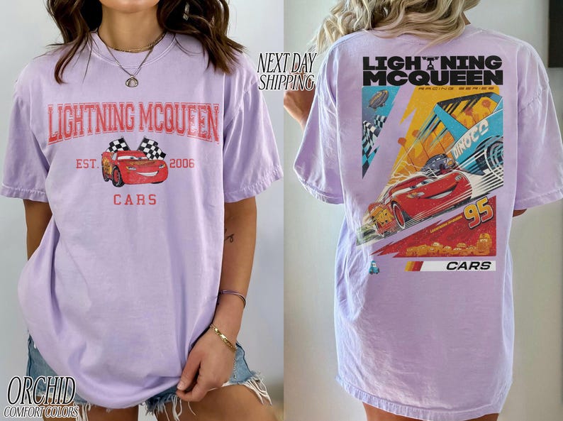 May include: Lavender t-shirt featuring Lightning McQueen from the Cars movie. The front graphic includes the text "Lightning McQueen" and "Cars", with a red race car and checkered flags. The back displays a larger graphic of McQueen racing.