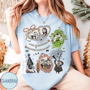May include: Light blue t-shirt featuring framed illustrations of characters from "The Nightmare Before Christmas." The design includes Jack Skellington, Sally, Oogie Boogie, and other characters, with the text "The Nightmare Before Christmas."