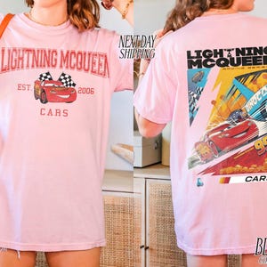 May include: Light pink t-shirt featuring Lightning McQueen from the Cars movie. The front graphic shows McQueen with checkered flags and text. The back displays a larger graphic of McQueen racing, with the number 95 and the word "CARS".