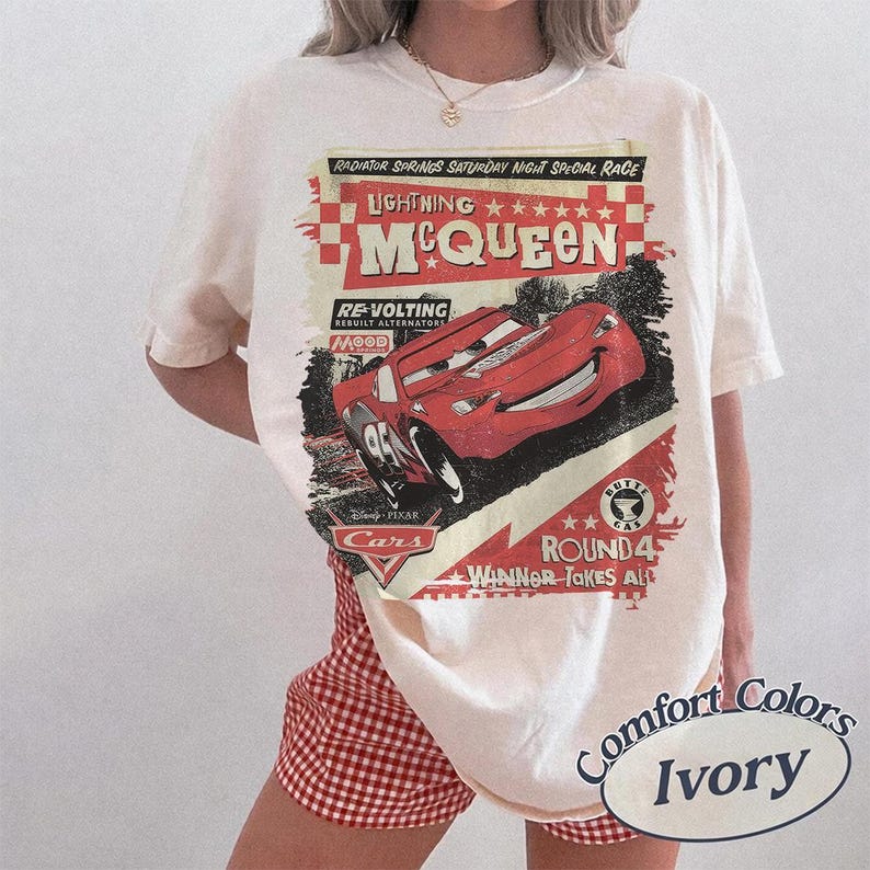 May include: Ivory-colored t-shirt featuring a graphic of Lightning McQueen from the Disney Pixar Cars movie. The design includes text that reads "Radiator Springs Saturday Night Special Race" and "Round 4 Winner Takes All."