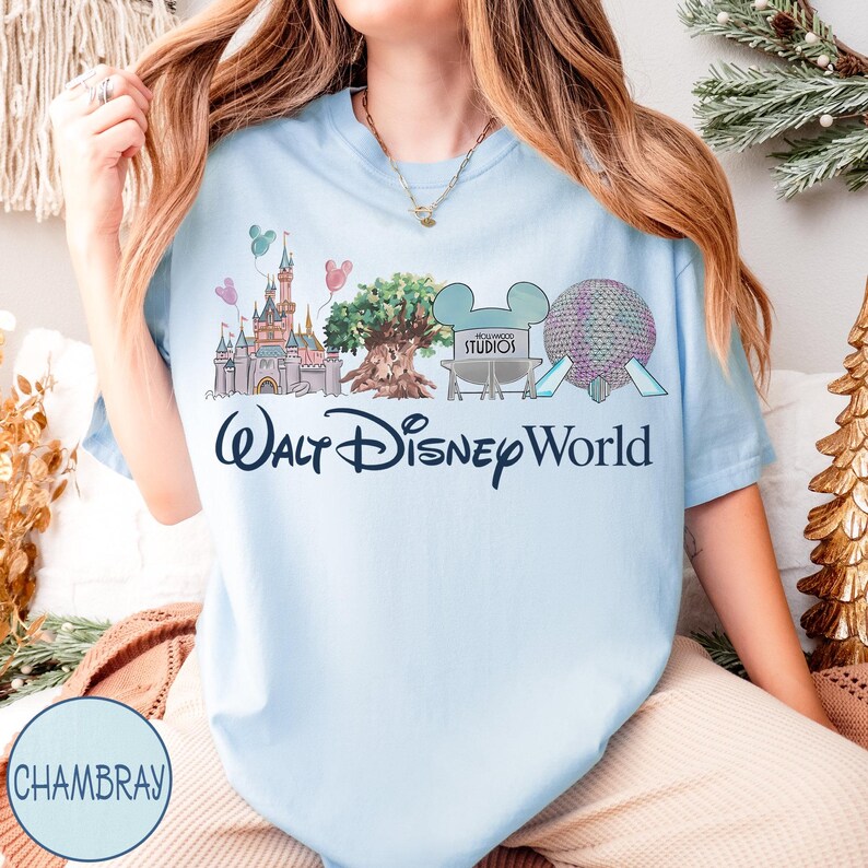 May include: Pale blue t-shirt with a graphic depicting Walt Disney World attractions, such as a castle, a tree, and Spaceship Earth. The words "Walt Disney World" are printed beneath the illustration. The shirt has short sleeves.