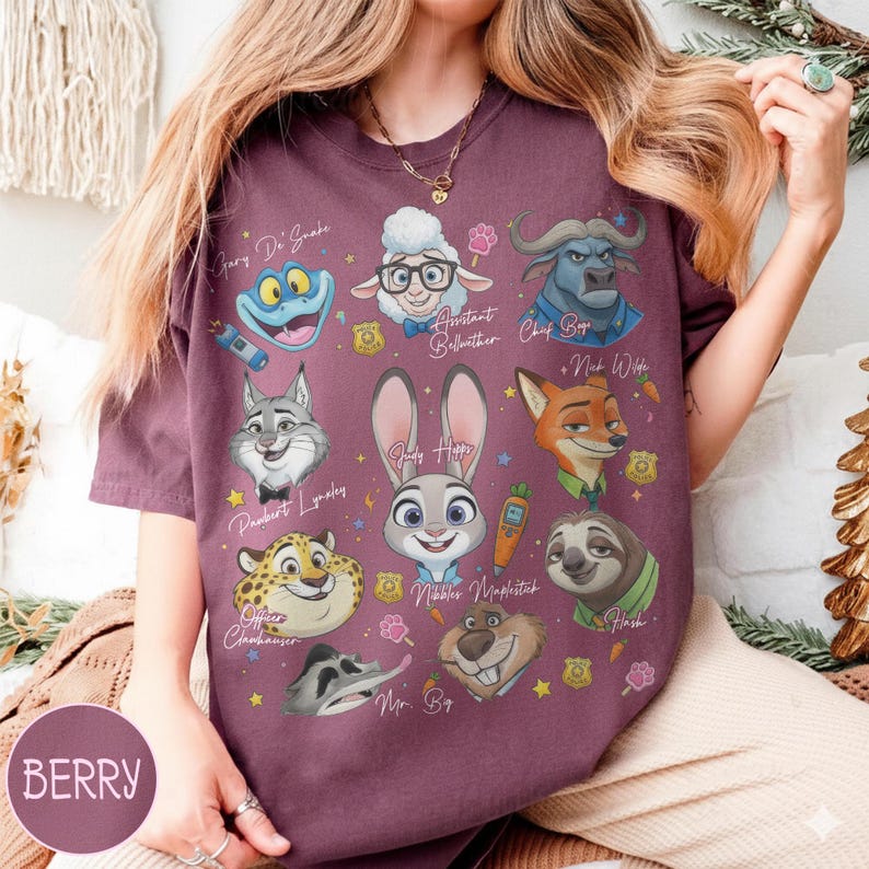 May include: Berry-colored t-shirt featuring cartoon characters from a movie. The shirt has illustrations of a frog, sheep, buffalo, wolf, rabbit, fox, sloth, and other characters. The text "BERRY" is in a circle on the bottom left.
