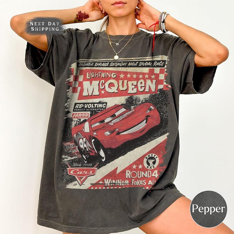 May include: Dark gray t-shirt featuring Lightning McQueen from the Disney Pixar Cars movie. The graphic includes the text "Lightning McQueen" and "Radiator Springs Saturday Night Special Race". The shirt also has the text "Round 4 Winner Takes All".