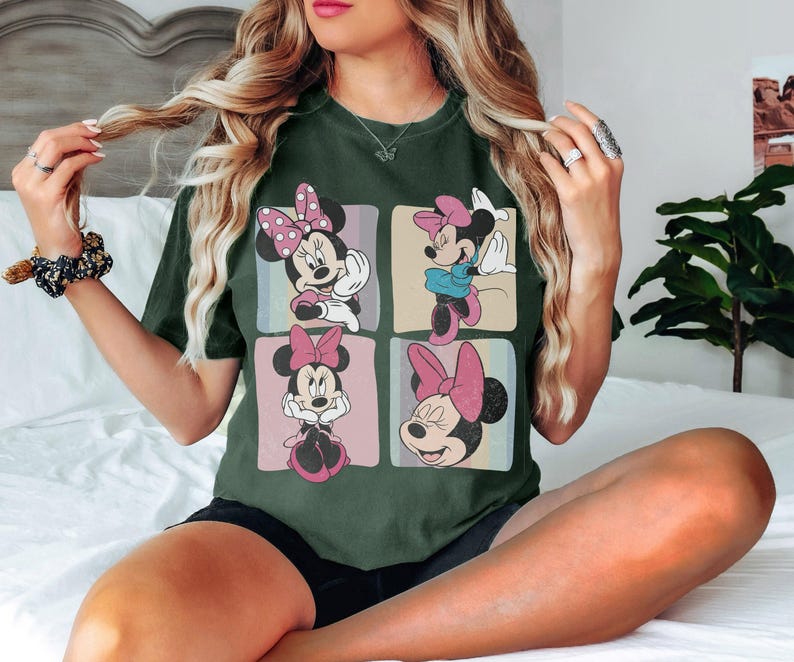 Op de afbeelding: Donkergroen t-shirt met vier panelen met Minnie Mouse-illustraties. Elk paneel toont een andere pose van Minnie Mouse, met haar kenmerkende strik en verschillende outfits. Het shirt is een comfortabele, casual stijl.