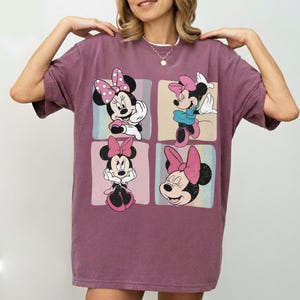 Op de afbeelding: Een mauvekleurig T-shirt met een ontwerp van vier panelen met Minnie Mouse in verschillende poses. Elk paneel heeft een andere achtergrondkleur en Minnie draagt haar kenmerkende roze strik en outfit. Het shirt heeft korte mouwen en een relaxte pasvorm.