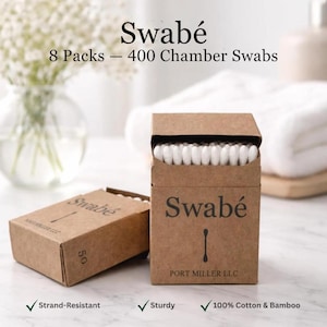 May include: Two open cardboard boxes of Swabé cotton buds. One box is upright, displaying the buds, and the other is lying down. The boxes are brown with the brand name and logo printed on them. The text reads "8 Packs - 400 Chamber Swabs".