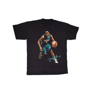 May include: Black t-shirt featuring a basketball player in a teal and black uniform, dribbling a basketball. The player's signature is in teal. The shirt has a vintage, slightly faded appearance.