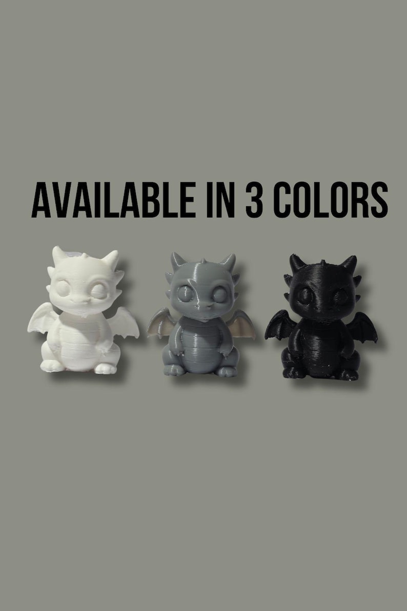 May include: Three small dragon figurines in white, gray, and black. Each creature features large eyes, pointed ears, and small wings. The text "AVAILABLE IN 3 COLORS" is printed in black above the figures, which are arranged in a horizontal row.