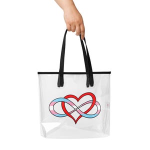 May include: Clear tote bag with black handles and trim. The bag features a red heart intertwined with a blue and pink infinity symbol, representing the transgender pride flag.