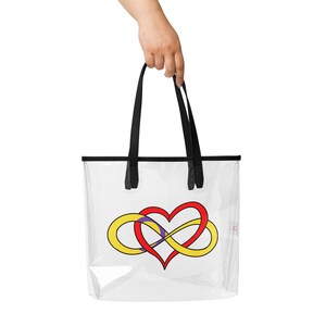 May include: Clear tote bag with black handles and trim. The bag features a colorful design of a red heart intertwined with a yellow infinity symbol and a purple accent. The bag is held by a hand.