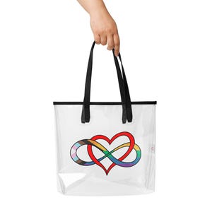 May include: Clear tote bag with black handles and trim. The bag features a colorful heart-shaped infinity symbol with rainbow and pride flag elements. The bag is held by a person.