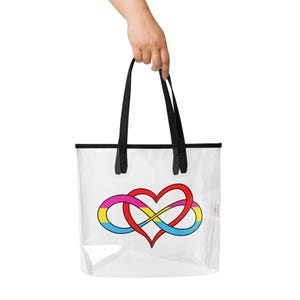 May include: Clear tote bag with black handles and trim. The bag features a colorful design of a heart intertwined with an infinity symbol, using the colors of the pansexual pride flag: pink, yellow, red, and blue. The bag is held by a hand.