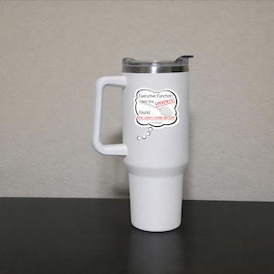 May include: A white travel mug with a black lid and a large handle. A sticker on the mug reads "Executive Function can't find SPOON(S) Found THE CRAFT STORE RECEIPT instead". The mug is on a black surface.