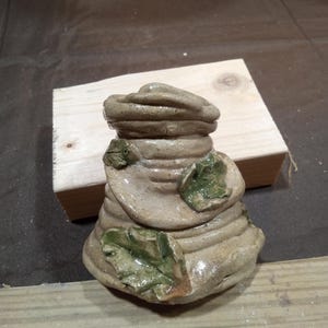 May include: A handmade wooden sign with the text "Welcome" in a handwritten style. The sign is painted white with a distressed finish, and a small green leaf is attached to the top. The sign measures approximately 12 inches wide.