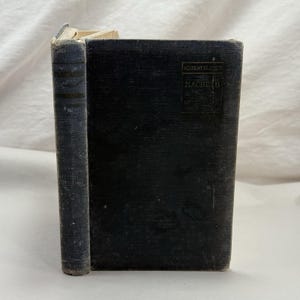 Op de afbeelding: Een donkerblauw hardcover boek met de titel Academy Classics Macbeth. De voorkant heeft een rechthoekig zwart label met gouden tekst. Het boek heeft een textielband met textuur en vertoont tekenen van slijtage langs de randen.