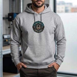 May include: A light gray hoodie with a front pocket and a drawstring hood. The hoodie features a circular graphic on the chest that reads "LIFE SUPPORT CREW" and "TRUST THE CHECKLIST" with an astronaut illustration. The hoodie is made of a soft material.