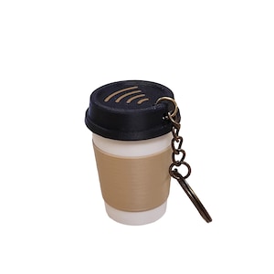 May include: A coffee cup keychain with a black lid and a tan sleeve. The keychain has a bronze-colored chain and key ring. The cup is white and appears to be made of plastic.