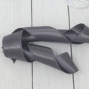 May include: A grey satin ribbon is curled and twisted on a white wooden surface.