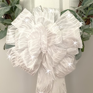 May include: A white, glittery bow with a wavy pattern. The bow is tied on a wreath.