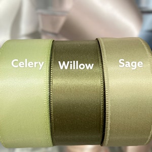 May include: Close-up of three spools of satin ribbon in shades of green: Celery, Willow, and Sage. The ribbon has a subtle sheen and a textured appearance. The names of the colors are printed in white on the ribbon.