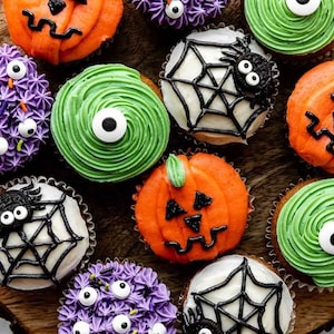 May include: A collection of Halloween-themed cupcakes featuring orange pumpkin faces, green swirls with single candy eyes, purple frosting with multiple candy eyes, and white frosting topped with black icing spiderwebs and small black spiders.