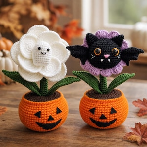 Pode incluir: Duas plantas de crochê em vasos laranja em forma de abóbora. A planta da esquerda apresenta uma flor branca com um pequeno fantasma no centro. A planta da direita apresenta uma flor roxa com um morcego preto no centro com presas.