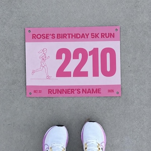 Könnte beinhalten: Eine rechteckige rosa Startnummer mit dem Text ROSE'S BIRTHDAY 5K RUN, der Zahl 2210, einer Läufergrafik und dem Text OCT 22 RUNNER'S NAME 2026. Unter der Startnummer befinden sich weiße Sportschuhe mit rosa Akzenten und weißen Socken.