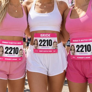 May include: Three athletic outfits consisting of pink or white racerback tank tops and matching shorts. Each outfit features a rectangular race bib pinned to the shorts, displaying the text EMMA'S BATCH CREW or BRIDE, the number 2210, and photos.