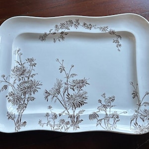 May include: A rectangular, off-white serving platter with a gently scalloped edge. The platter is decorated with a brown floral pattern featuring chrysanthemums and other flowers. The design is concentrated around the edges.