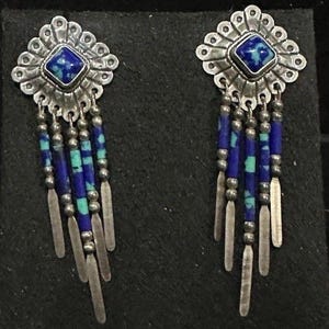 Könnte beinhalten: Ein Paar silberne Ohrhänger mit einem quadratischen blau-türkisfarbenen Stein in einer gewellten Metallfassung. Jeder Ohrring hat vier hängende Stränge aus abwechselnden blauen und türkisfarbenen Perlen, silbernen Kugeln und flachen Silberenden.