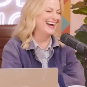 May include: A light-colored laptop featuring a square sticker with the text GOOD HANG in a colorful geometric pattern, placed next to a white ceramic mug with a matching geometric design, a black microphone, and a person wearing a purple jacket.