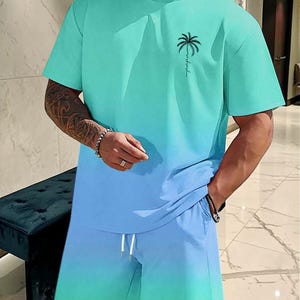 May include: A two-piece matching set in a gradient teal and blue color scheme. The short-sleeved t-shirt features a palm tree graphic and the shorts have a drawstring waist. The outfit is made of a soft, comfortable material.