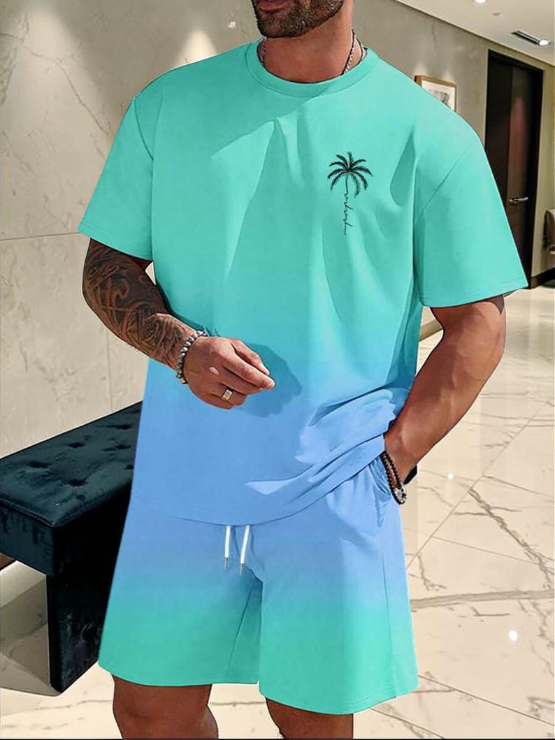 May include: A two-piece matching set in a gradient teal and blue color scheme. The short-sleeved t-shirt features a palm tree graphic and the shorts have a drawstring waist. The outfit is made of a soft, comfortable material.