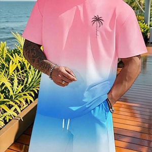 May include: A two-piece set featuring a pink and blue gradient design. The short-sleeved t-shirt has a palm tree graphic and the word "relax" printed on the chest. The shorts have a drawstring waist. The set is made of a soft, comfortable material.
