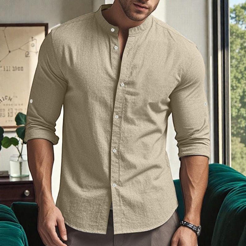 May include: A beige long-sleeve shirt with a mandarin collar and button-down front. The shirt has buttoned cuffs and is made of a lightweight fabric. The shirt is a neutral color and suitable for casual wear.