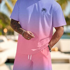 May include: A two-piece outfit featuring a gradient design. The top is a short-sleeved t-shirt with a palm tree graphic and the shorts have a drawstring. The color scheme transitions from purple to pink.