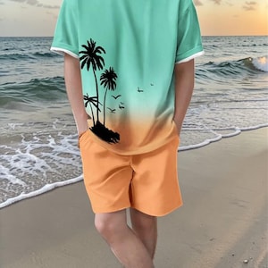 May include: A two-piece beach set featuring a teal and orange gradient t-shirt with a black palm tree graphic and orange shorts. The t-shirt has white trim on the sleeves and neckline. The person is standing on a sandy beach.