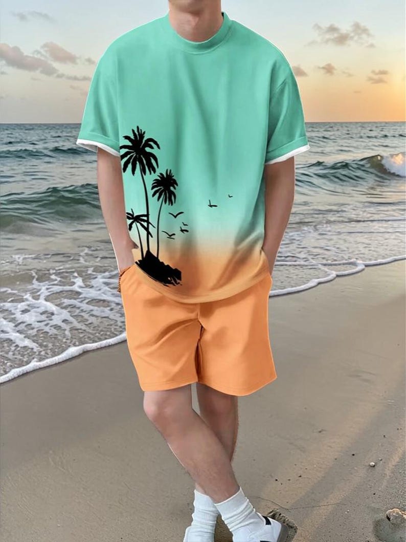 May include: A two-piece beach set featuring a teal and orange gradient t-shirt with a black palm tree graphic and orange shorts. The t-shirt has white trim on the sleeves and neckline. The person is standing on a sandy beach.