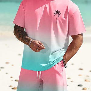 May include: A two-piece set featuring a pink and teal ombre design. The set includes a short-sleeved t-shirt with a palm tree graphic and matching shorts with a drawstring. The outfit is perfect for a beach day.